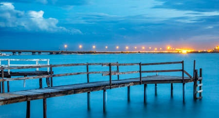 Long exposure of an old jetty on a river with city lights in the backgroundの写真素材