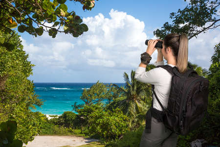 Pretty Young Lady Hiker with Binoculars and Backpack at the Coastの写真素材