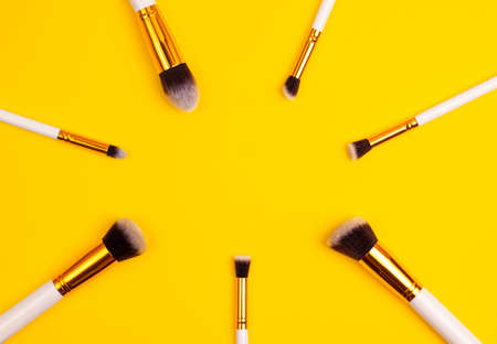 Template top view of gold colored  cosmetics white brushes set for makeup  on bright yellow background. Cosmetics and beauty concept template Make up concept with copy space flat layの写真素材