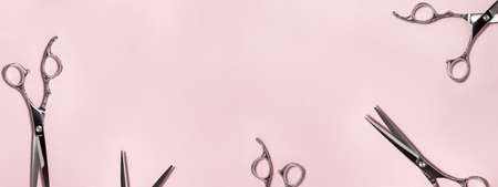 Banner flat lay from above of professional silver hair cutting shears set on pink background. Hairdresser salon equipment and haircut work tools concept during quarantine with copy space.の写真素材