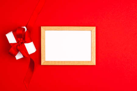 Mockup wooden frame flat lay of white gift box with a red satin ribbon bow on the left on vibrant red background. Mothers day holiday presents happy birthday concept with space for your textの写真素材