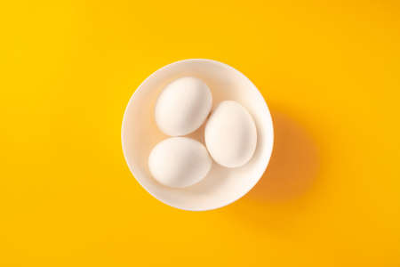 Three white eggs in a bowl on yellow background.の写真素材