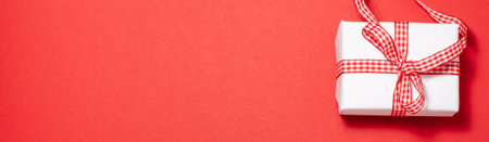 Banner of white gift box with a red ribbon bow  on the right side on red background. Flat lay top view with space for text. Presents and holidays conceptの写真素材