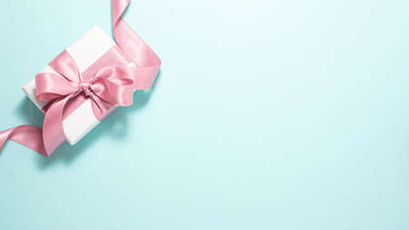 White paper gift box with a purple satin ribbon bow aon the left side on blue background. Valentines day, gift and holidays concept from above. Flat lay top view with copy spaceの写真素材