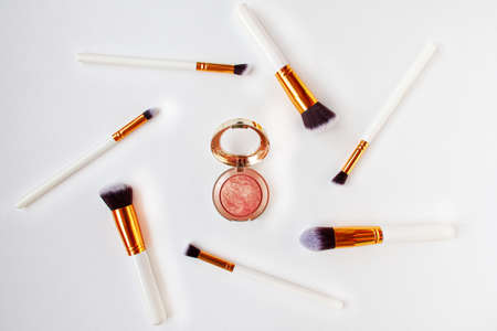 Flat lay top view of female cosmetics brushes set for makeup and opened rouge in the middle on white...