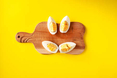 One white egg on a wooden cutting board is cut into quarters, which represent a smile on yellow background. World egg day conceptの写真素材
