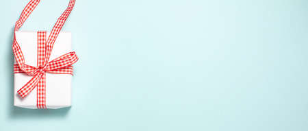 Banner of white gift box with a red ribbon bow on left side on blue background. Flat lay top view...