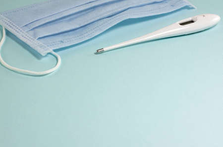 White thermometer, mask at the top of the frame on a blue background with copy space.