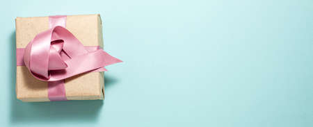 Banner of brown paper gift box with a purple satin ribbon on the left side of the frame bow on blue background. Flat lay top view. Gift andholidays concept from above with copy spaceの写真素材