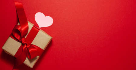 One pink heart near the brown paper gift box with a red ribbon bow on the left side of the frame....
