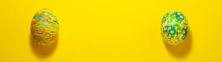 Banner of two easter colorful eggs roll out to each other on yellow background. Flat lay with copy...