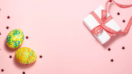 Yellow and green Easter eggs, white gift box with red ribbon bow and red stars on pink background...