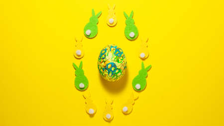 Yellow and green velvet bunnies and Easter egg in the center of the frame on a yellow background....