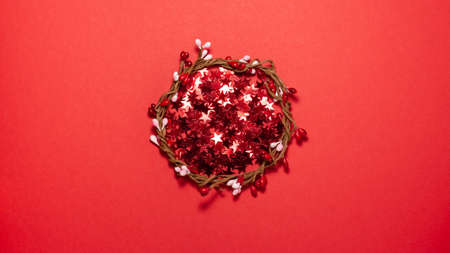 Woven wreath with red and pink buds on red background at the center of the frame. Flat lay top view....