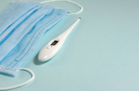 White thermometer, mask at the left of the frame on a blue background with copy space.
