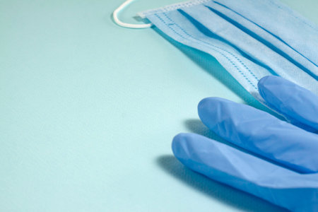 Blue mask and medical glove on the right side of the frame on a blue background with copy space.
