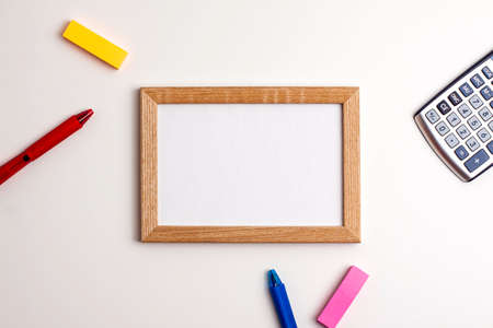 Yellow and pink sticky note, wooden frame, red and blue pen calculator on white background. Flat lay...