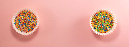 Cupcake liners with colored sugar inside on the left and right from above. Flat lay top view. Confectionery cooking concept with copy space on bright pink paper background bannerの写真素材