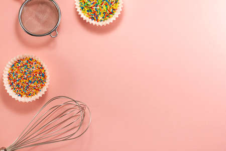 Cupcake liners with colored sugar inside whisk and strainer from above. Flat lay top view. Confectionery cooking concept with copy space on bright pink paper backgroundの写真素材