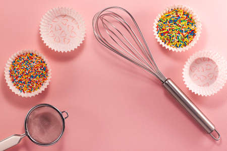 Cupcake liners with colored sugar inside whisk and strainer from above. Flat lay top view. Confectionery cooking concept with copy space on bright pink paper backgroundの写真素材