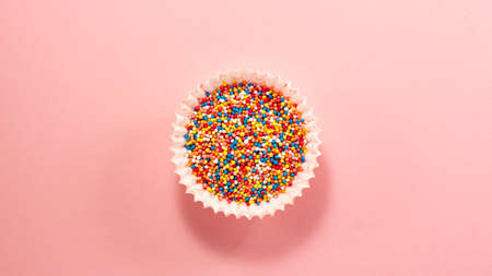 Cupcake liners with colored sugar inside from above. Flat lay top view. Confectionery cooking concept with copy space on bright pink paper backgroundの写真素材