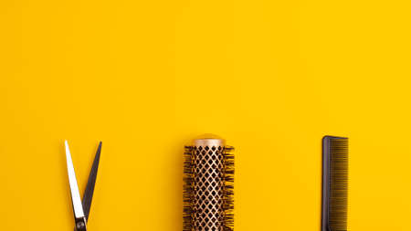 Banner template flat lay of professional hair cutting shears comb for separating hair and gold round hair brush for styling on yellow background Hairdresser salon equipment concept with copy spaceの写真素材