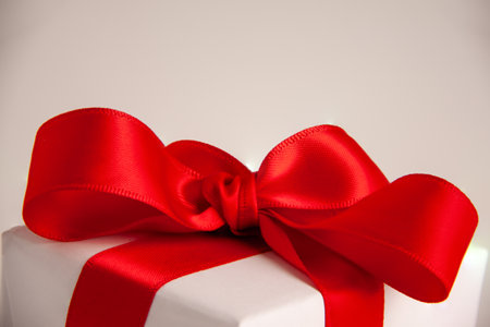 Close up of white paper gift box with a red satin ribbon bow on bright background. Holidays greeting cards and Christmas shopping concept with copy space.の写真素材