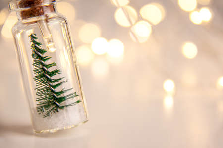 Close up of glowing lights decoration of glass jars with corks inside which there are small green Christmas trees on artificial snow. Holidays New Year concept with copy space and bokeh on leftの写真素材