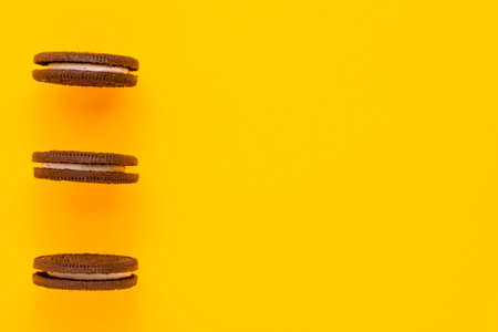 Sweet brown cookies with white cream inside on bright yellow background at the left. Close up with copy space. Homemade and bakery conceptの写真素材