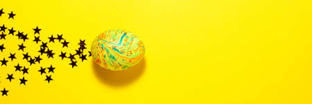 Easter colorful egg flies through the frame leaving stars behind itself on yellow background. Flat lay with copy space bannerの写真素材