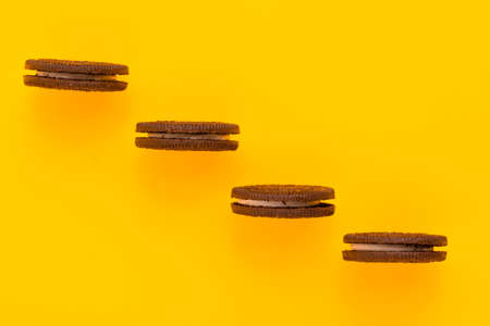 Sweet brown cookies with white cream inside on bright yellow background. Close up with copy space. Homemade and bakery conceptの写真素材