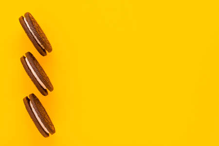 Sweet brown cookies with white cream inside on bright yellow background at the left. Close up with copy space. Homemade and bakery conceptの写真素材