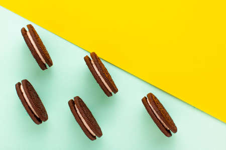 Sweet brown cookies with white cream inside on bright yellow and blue background. Close up with copy space. Homemade and bakery conceptの写真素材