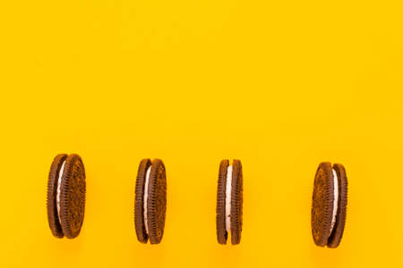 Sweet brown cookies with white cream inside on bright yellow backgroundat the bootom. Close up with copy space. Homemade and bakery conceptの写真素材