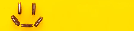 Sweet brown cookies smile with white cream inside on bright yellow background. Close up with copy space. Homemade and bakery concept bannerの写真素材