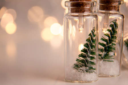 Close up of glowing lights decoration of glass jars with corks inside which there are small green Christmas trees on artificial snow. Holidays New Year concept with copy space and bokeh on rightの写真素材