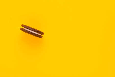 Sweet brown cookie with white cream inside on bright yellow background. Close up with copy space. Homemade and bakery conceptの写真素材