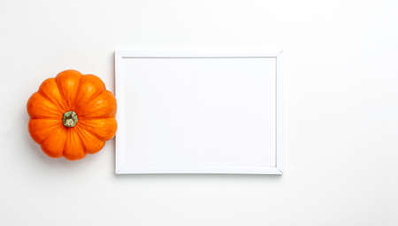 Mock up flat lay of mini decorative orange pumpkin and white frame on bright background from above at the top. Halloween and Thanksgiving greeting card holiday concept with copy spaceの写真素材