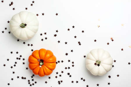 Flat lay of mini decorative white and orange pumpkin and brown stars on bright background from above. Halloween and Thanksgiving greeting card holiday concept with copy spaceの写真素材