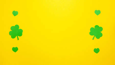 Green clovers and green heart on the left and right side flat lay top view on yellow background with copy space. Saint Patrick Day conceptの写真素材