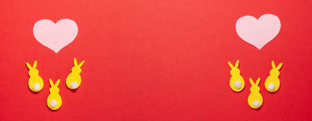 Yellow velvet bunnies and pink hearts banner on red background at the battom with copy space. Flat lay top view. Easter concept.の写真素材