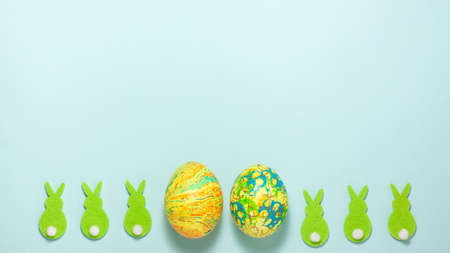 Green rabbits and easter egg at the bottom on blue background. Flat lay top view with copy spaceの写真素材