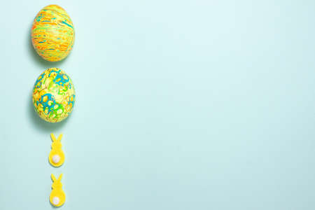 Yellow rabbits and green easter egg on the left side on blue background. Flat lay top viiew with copy spaceの写真素材