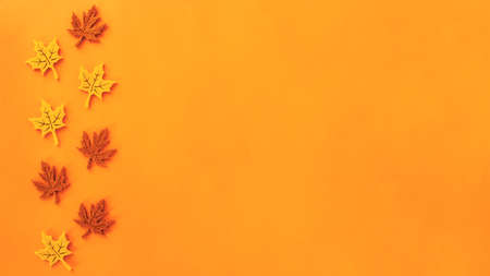 Beautiful autumn flat lay banner of felt decoration leaves of yellow and red maple at the left on orange background. Holidays concept with copy spaceの写真素材