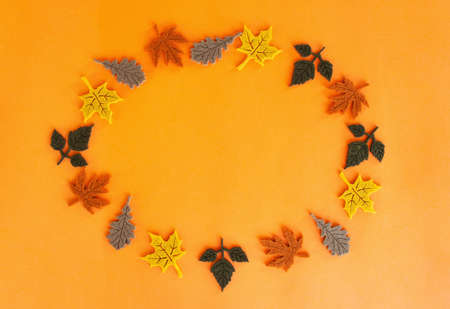 Beautiful autumn flat lay of felt decoration leaves of oak and maple of yellow red orange green and brown colors standing in a circle and spinning around its axis on orange backの写真素材
