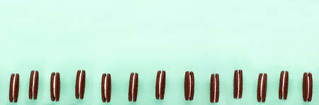 Sweet brown cookies with white cream inside on bright blue background at the bottom. Close up with copy space. Homemade and bakery concept bannerの写真素材