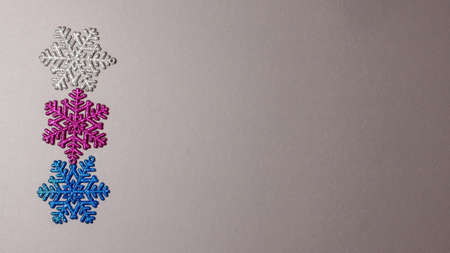 Tree snowflakes of silver, blue and purple colors with glitter dancing on gray paper background of the left side. Flat lay top view with copy space Christmas holidays conceptの写真素材