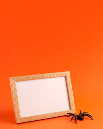 Close up of mockup template white frame with wooden borders and black horror spider on orange blurred background and copy space. Holiday autumn concept backdrop.の写真素材