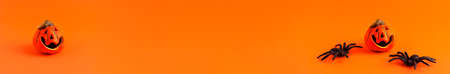 Close up banner of decoration orange small smile Halloween pumpkin and black horror spiders on orange blurred background and copy space. Holiday autumn concept backdropの写真素材