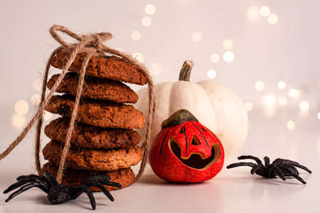 Close up of oatmeal cookies in a stack tied with brown thread and halloween black spiders white and orange small pumpkin on bright background with bokeh. Sweet food concept with copy spaceの写真素材